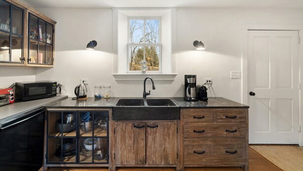 A kitchen with a large island, wooden cabinets, a microwave, a coffee maker, and a window above the sink.