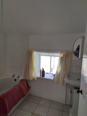 A bathroom with a bathtub, a window with curtains, a sink, and a mirror. - Lovely 4-bed Apartment in Mullaghbawn Newry (Newry)
