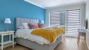Una camera da letto con un letto, comodini, una lampada, una sedia e una finestra con persiane.