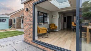 Una casa moderna con una porta in vetro che si apre su un patio con sedie gialle e un tavolo di legno.