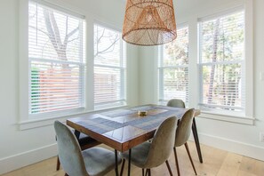 A dining area with a wooden table, four grey chairs, and a woven pendant light. - Modern 30A Grayton Beach Retreat | 5 min to beach | 4 Bikes | Huge Pool! (Santa Rosa Beach)
