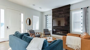 Un salon moderne avec un canapé bleu, un canapé marron et une table basse. On y trouve une cheminée, un téléviseur et une fenêtre avec des stores.