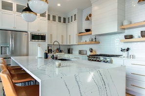 A modern kitchen with white cabinetry, a large marble island, stainless steel appliances, and a gas stove.