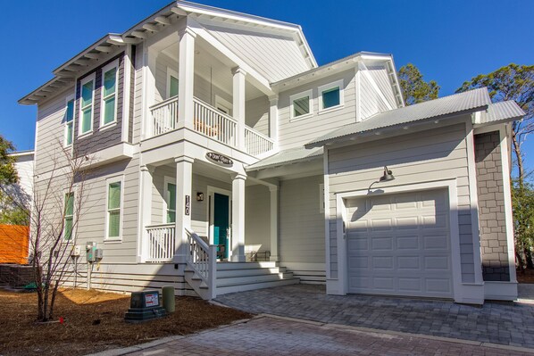 A two-story house with a front porch, a garage, and a small front yard. - Modern 30A Grayton Beach Retreat | 5 min to beach | 4 Bikes | Huge Pool! (Santa Rosa Beach)