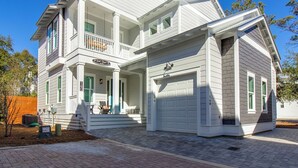 Une maison à deux étages avec un porche à l’avant, un garage et un petit espace extérieur aménagé pour s’asseoir.