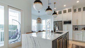 Une cuisine moderne avec des meubles blancs, un îlot en marbre et des luminaires suspendus.