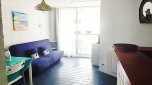 Ein Zimmer mit einem blauen Sofa, einem Tisch mit Stühlen, einer hölzernen Bank und Blick ins Freie.