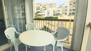 Ein Balkon mit einem weißen Tisch und vier weißen Stühlen, mit Blick auf ein Wohngebiet mit Gebäuden.