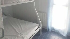 Ein Schlafraum mit Etagenbetten, Heizkörper und einem Vorhangfenster.