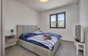 Une chambre à coucher avec un lit, une table de chevet, un téléviseur et une fenêtre donnant sur la ville.