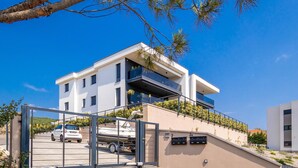 A modern two-story building with a flat roof, a balcony on the upper floor, and a gated entrance with a white car parked inside. - Nice Apartment in Kostrena With 3 Bedrooms and Wifi (Kostrena)