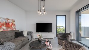 A modern living room with a grey sofa, a round coffee table, and a TV on a white cabinet. - Nice Apartment in Kostrena With 3 Bedrooms and Wifi (Kostrena)