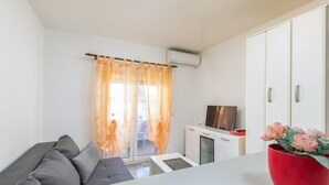 Een moderne woonkamer met een grijze bank, een flatscreen televisie en een rode vaas met bloemen.