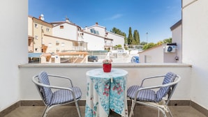 Een balkon met twee stoelen en een tafel, met uitzicht op een woongebied met gebouwen en bomen.