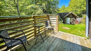 A wooden deck with a table and two chairs, overlooking a grassy area with a small wooden structure. - Amazing Home in Mollaryd With 2 Bedrooms and Wifi (Ljung)