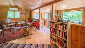 A cozy cabin interior with a wooden interior, a dining area, a seating area with a red blanket, and a bookshelf filled with books. - Amazing Home in Mollaryd With 2 Bedrooms and Wifi (Ljung)