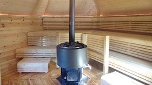 A wooden sauna with a central heating unit, benches, and a sloped ceiling. - Awesome Home in Huskvarna With 3 Bedrooms, Jacuzzi and Wifi (Huskvarna)
