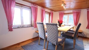 Un coin repas avec une table en bois, quatre chaises et des rideaux à carreaux rouges et blancs.