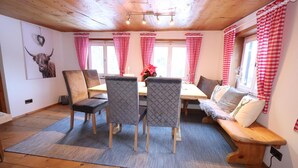Un coin repas accueillant avec une table et des chaises en bois, un banc avec des coussins et des rideaux à carreaux rouges et blancs.