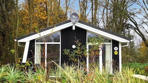 Una piccola cabina nera con un’antenna parabolica con la scritta "Wisi Orbit" sul tetto, circondata da erba alta e alberi.