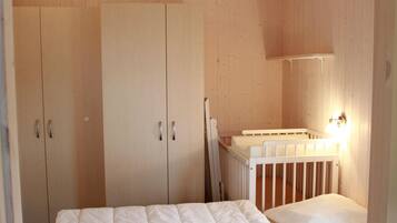 A bedroom with a crib, wooden wardrobe, and a wall-mounted light.