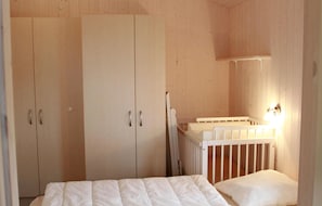 Un dormitorio con una cuna, un armario de madera y una lámpara fijada a la pared.