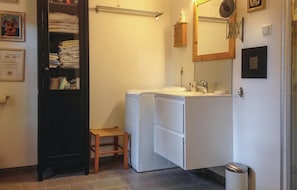 A compact bathroom with a washing machine, a small stool, a towel rack, and a mirror.