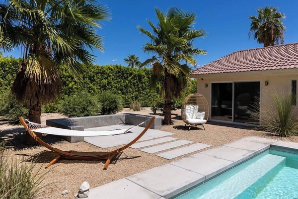 Sunlit backyard oasis — pool, hammock stand, sunken hot tub, and egg chair tucked among tall palms and privacy hedges