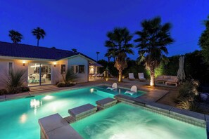 A swimming pool with lounge chairs and a patio area, surrounded by palm trees.