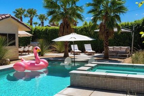 A swimming pool with a pink flamingo float, lounge chairs, and palm trees.
