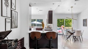Een moderne keuken met een centraal eiland, barkrukken en een eethoek met stoelen.