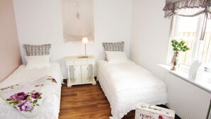 A bedroom with two single beds, a bedside table with a lamp, a radiator, and a window with a plant. - Beautiful Apartment in Kungshamn With 3 Bedrooms and Wifi (Kungshamn)