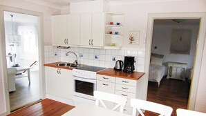 A compact kitchen with white cabinets, a stove, and a coffee maker. There is a dining area with a table and chairs. - Beautiful Apartment in Kungshamn With 3 Bedrooms and Wifi (Kungshamn)