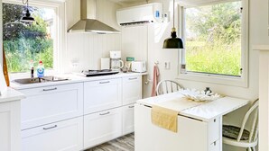 Eine moderne Küche mit weißen Schränken, einem Backofen, einer Kaffeemaschine und einem Fenster mit Blick auf Grünflächen.