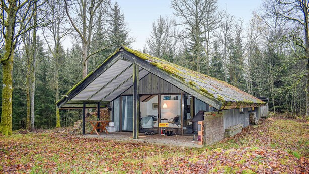 Eine rustikale Holzhütte mit geneigtem Dach, einer Veranda und einem großen Fenster.