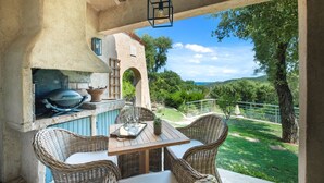 Eine Terrasse im Freien mit Korbmöbeln, einem Grill und Blick auf die Landschaft.