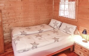 A wooden cabin room with a bed featuring star-patterned bedding, a nightstand with a lamp, and a window with curtains. - Awesome Home in Deutschlandsberg With 1 Bedrooms and Wifi (Deutschlandsberg)