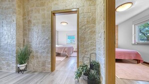 A room with stone walls, a wooden floor, and a bed with a pink bedspread. There are potted plants and a window with a view. - Stone House Captivating Villa in Pridraga, Zadar (Novigrad)