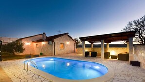 A swimming pool with stone tiles, a covered patio with seating, and a building with a sloped roof. - Stone House Captivating Villa in Pridraga, Zadar (Novigrad)