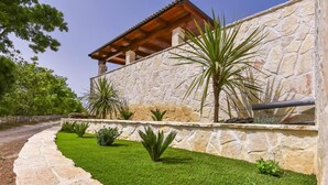 A stone building with a wooden pergola, a stone wall, and a well-maintained lawn with various plants. - Stone House Captivating Villa in Pridraga, Zadar (Novigrad)