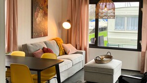 A modern living room with a sofa, yellow chairs, a dining table, a pendant light, and a view of a house through a window. - Stunning Home in Breukelen With 2 Bedrooms and Wifi (Breukelen)
