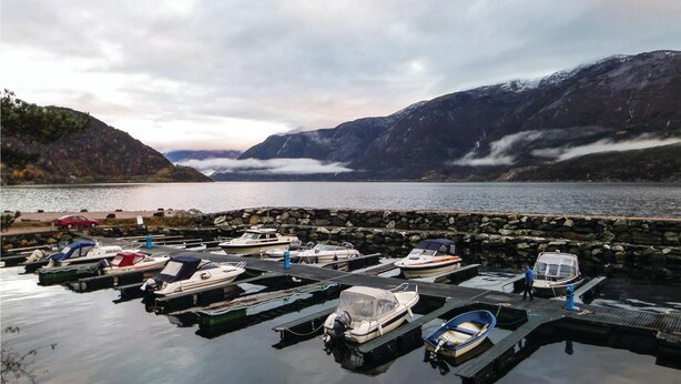 Un port de plaisance où sont amarrés des bateaux, entouré de montagnes et bordé par un lac.