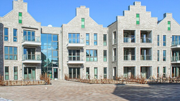 Un immeuble moderne à plusieurs étages, doté d’une façade en briques, de grandes fenêtres et de balcons.