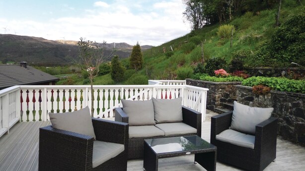 An outdoor patio with wicker furniture and a glass table, overlooking a hillside with wind turbines and greenery. - Nice Apartment in Fitjar With 2 Bedrooms and Wifi (Fitjar)