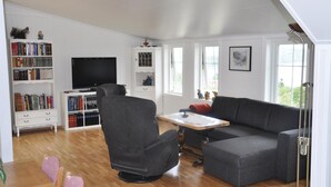 A spacious living room with a grey sofa, a television, and a bookshelf filled with books. - Nice Apartment in Fitjar With 2 Bedrooms and Wifi (Fitjar)