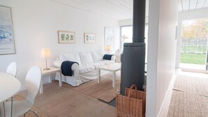 A modern living room with a white sofa, a white coffee table, and a black heater. There are framed pictures on the wall and a lamp on a side table. - Awesome Home in Burgsvik With 3 Bedrooms and Wifi (Burgsvik)