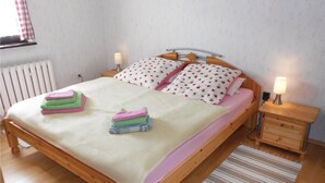 A wooden bed with a white and pink bedspread, two pillows with a floral pattern, and a bedside table with a lamp. - Amazing Apartment in Koserow With 2 Bedrooms and Internet (Koserow)