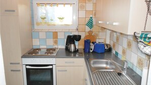 A compact kitchen with a stove, oven, sink, and a window with a floral curtain. - Amazing Apartment in Koserow With 2 Bedrooms and Internet (Koserow)