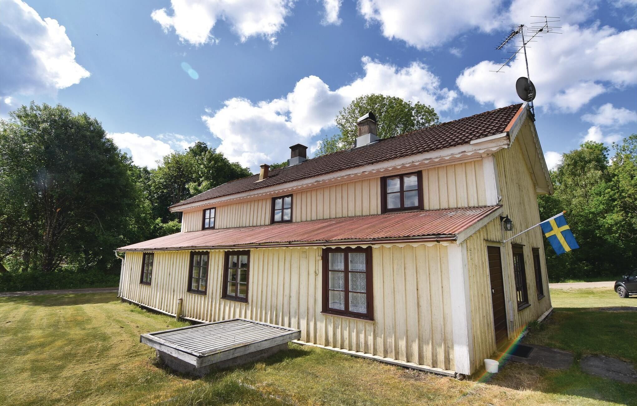 A two-story wooden house with a red-tiled roof, a small porch, and a flag.