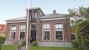 Een twee verdiepingen tellend bakstenen huis met een zwarte voordeur, grote ramen en een klein portaal met een bankje.